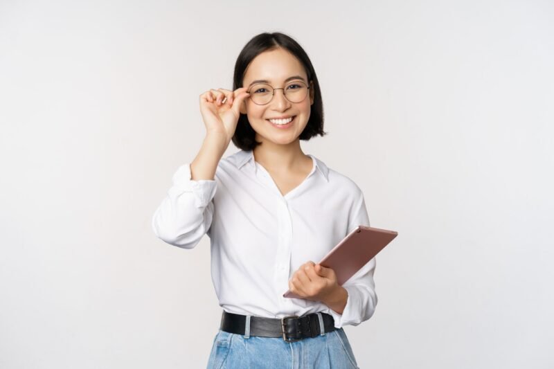 Image of young asian business woman, female entrepreneur in glasses, holding tablet and looking professional in glasses, white background.